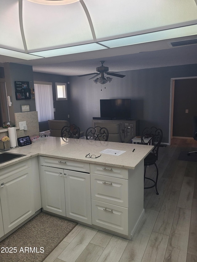 kitchen with white cabinetry, light stone counters, light wood-type flooring, and kitchen peninsula