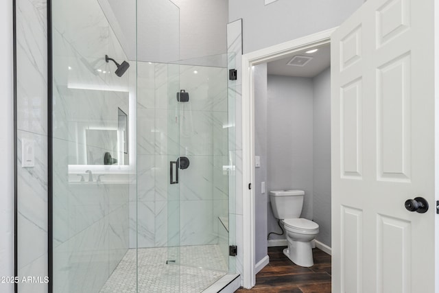 bathroom with hardwood / wood-style flooring, a shower with shower door, and toilet