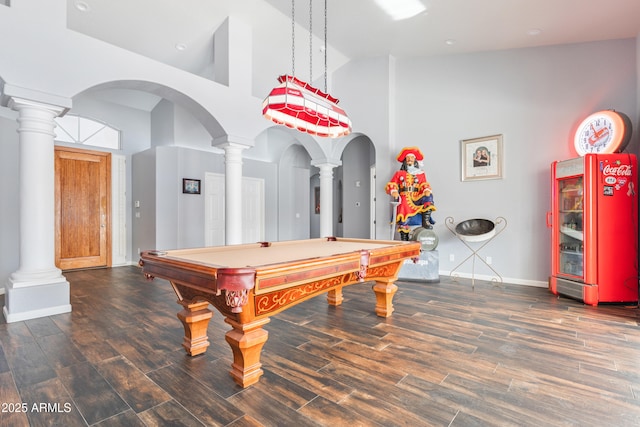 playroom featuring a towering ceiling, dark hardwood / wood-style flooring, and ornate columns