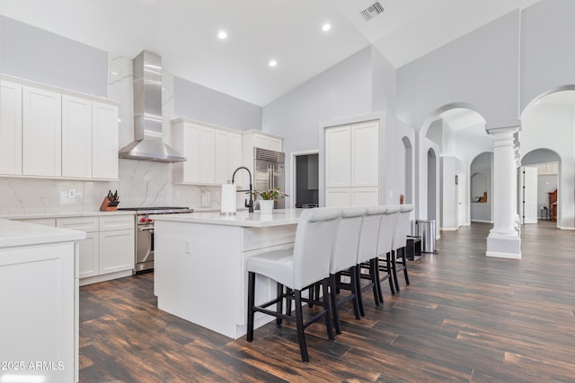 kitchen with white cabinetry, wall chimney exhaust hood, a kitchen island with sink, and premium appliances