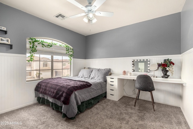 carpeted bedroom featuring a ceiling fan, visible vents, and wainscoting