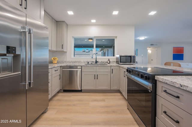 kitchen with light stone countertops, appliances with stainless steel finishes, sink, and light hardwood / wood-style floors