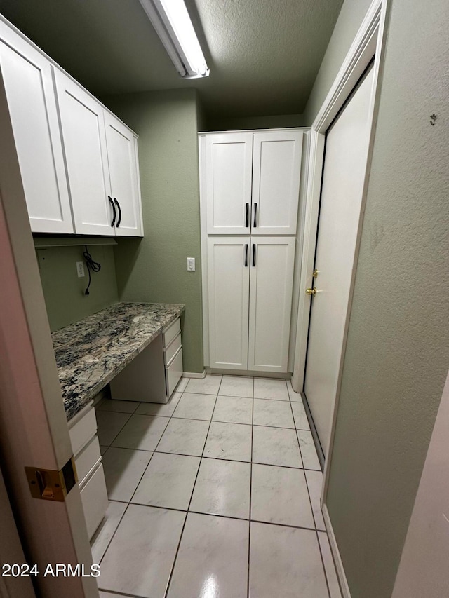 clothes washing area with a textured ceiling and light tile patterned floors