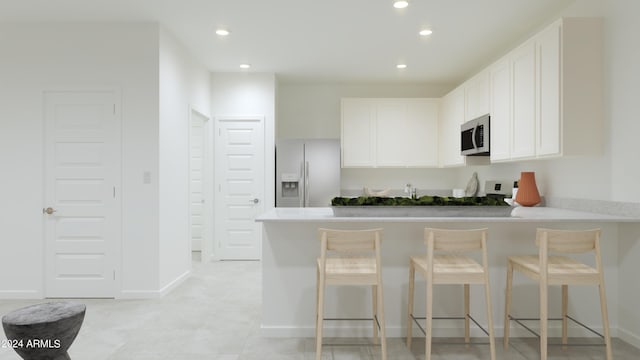 kitchen with a peninsula, recessed lighting, white cabinets, stainless steel microwave, and refrigerator with ice dispenser