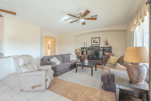 living room featuring arched walkways, ceiling fan, wood finished floors, and visible vents