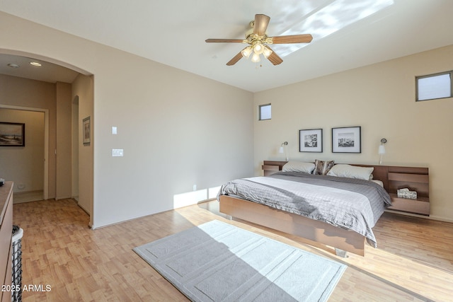 bedroom with arched walkways, light wood-type flooring, and a ceiling fan