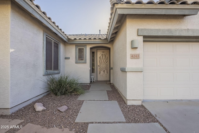 property entrance with an attached garage, a tile roof, and stucco siding