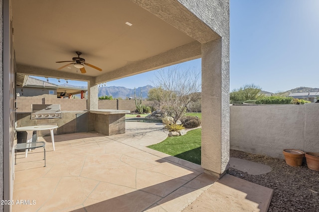 view of patio / terrace featuring area for grilling, fence, a mountain view, and a ceiling fan