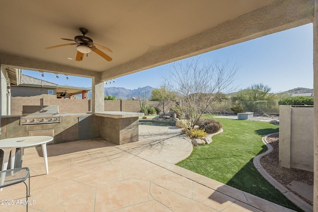 view of patio / terrace with ceiling fan, a fenced backyard, a mountain view, exterior kitchen, and grilling area