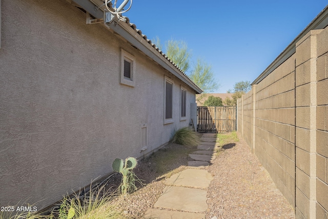 view of side of home featuring a fenced backyard, a tiled roof, and stucco siding