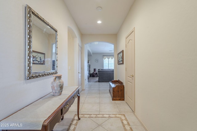 corridor with light tile patterned floors, baseboards, arched walkways, and recessed lighting