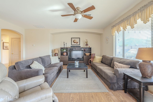 living area with light wood-style flooring, visible vents, arched walkways, and a ceiling fan