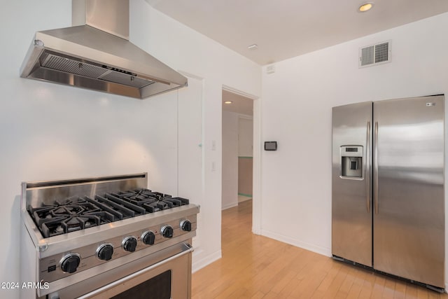 kitchen featuring wall chimney range hood, stainless steel appliances, and light wood-type flooring