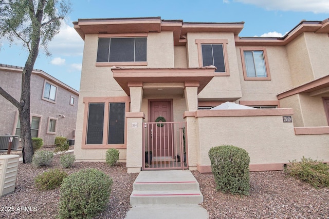 view of property featuring stucco siding, central air condition unit, a fenced front yard, and a gate