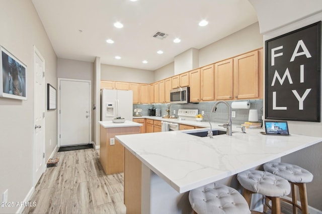 kitchen featuring electric stove, stainless steel microwave, white fridge with ice dispenser, light brown cabinets, and a sink