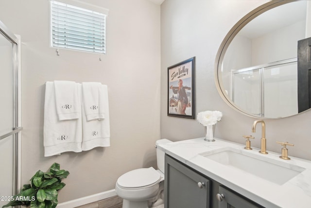 bathroom with toilet, vanity, baseboards, and a shower with shower door