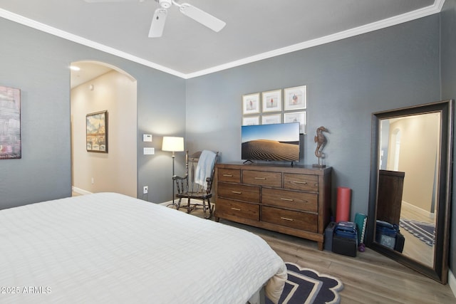 bedroom featuring baseboards, arched walkways, ceiling fan, wood finished floors, and crown molding