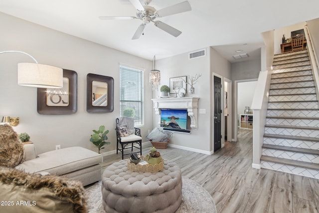 living area with light wood finished floors, visible vents, a glass covered fireplace, baseboards, and stairs