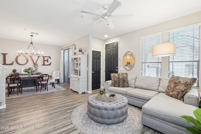 living room featuring light wood-style floors, visible vents, and ceiling fan with notable chandelier