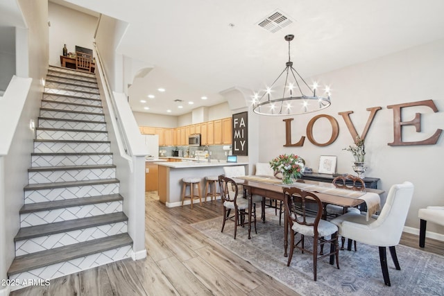 dining room with light wood finished floors, stairway, visible vents, and a notable chandelier