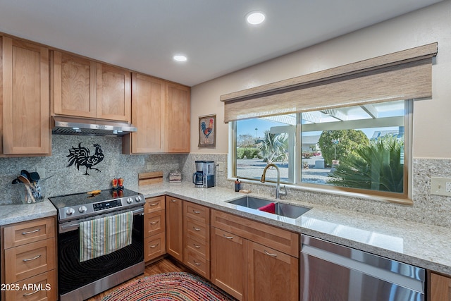 kitchen with sink, appliances with stainless steel finishes, hardwood / wood-style floors, light stone counters, and tasteful backsplash