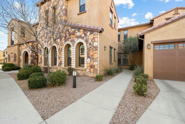 view of front of house featuring a garage, stone siding, a tiled roof, and stucco siding