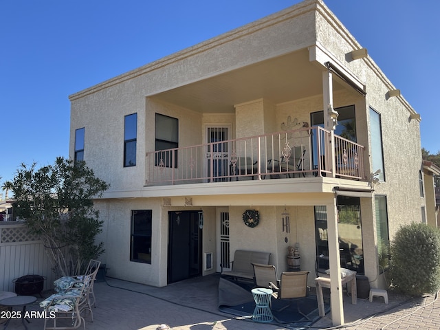 rear view of house featuring stucco siding, fence, a fire pit, a balcony, and a patio area