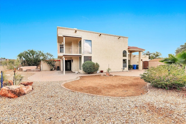 rear view of house with a balcony, a patio area, fence, and stucco siding