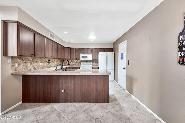 kitchen with white appliances, visible vents, a peninsula, a sink, and tasteful backsplash