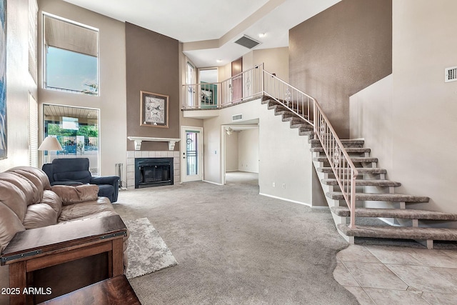 carpeted living room featuring visible vents, a high ceiling, a tiled fireplace, and stairway