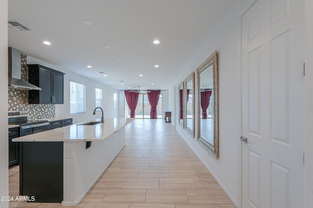 kitchen with a breakfast bar, a center island with sink, stainless steel electric stove, sink, and wall chimney exhaust hood