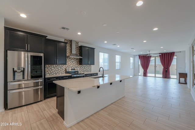 kitchen featuring a center island with sink, a kitchen breakfast bar, sink, wall chimney exhaust hood, and appliances with stainless steel finishes