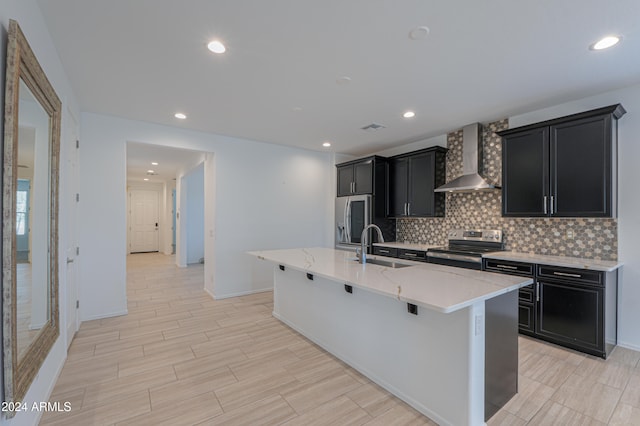 kitchen with appliances with stainless steel finishes, a breakfast bar, a kitchen island with sink, sink, and wall chimney range hood