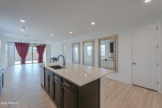 kitchen with light stone counters, stainless steel dishwasher, ceiling fan, sink, and an island with sink