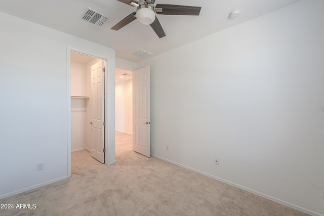 unfurnished bedroom featuring ceiling fan, light colored carpet, a walk in closet, and a closet