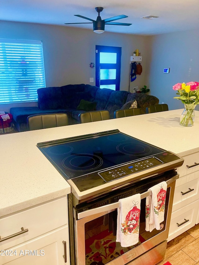 kitchen featuring ceiling fan, white cabinetry, stainless steel electric range oven, and light hardwood / wood-style flooring