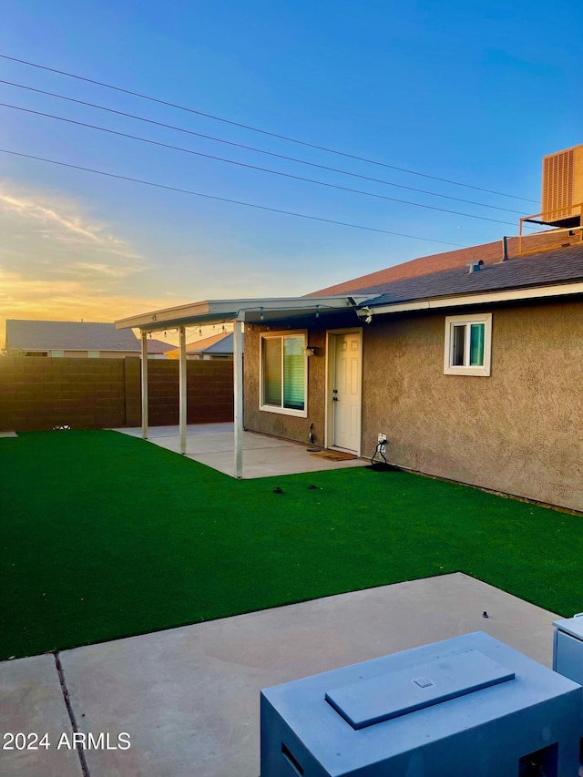 back house at dusk with a yard, a patio, and central AC