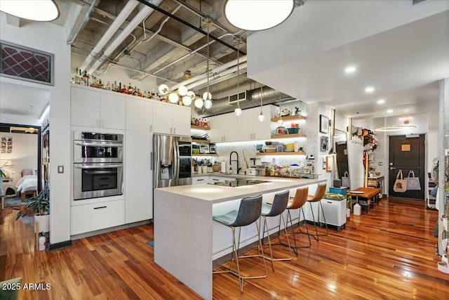 kitchen featuring appliances with stainless steel finishes, wood-type flooring, hanging light fixtures, white cabinets, and a breakfast bar area