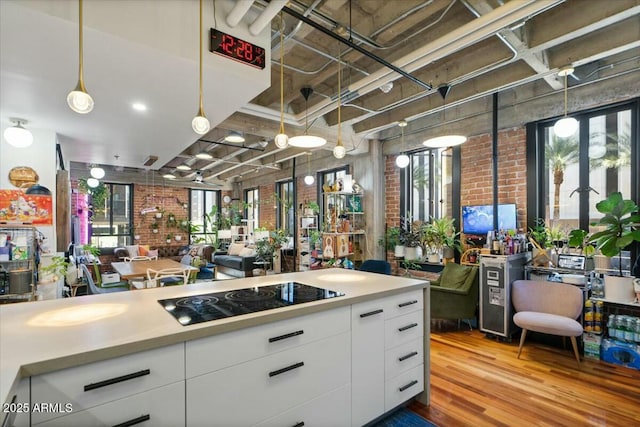 kitchen with decorative light fixtures, white cabinetry, brick wall, black electric cooktop, and light hardwood / wood-style floors