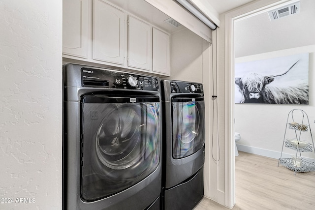 clothes washing area featuring washer and dryer, light hardwood / wood-style flooring, and cabinets