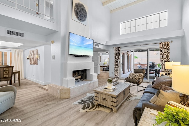 living room with a high ceiling, light hardwood / wood-style flooring, beamed ceiling, wood ceiling, and a tiled fireplace