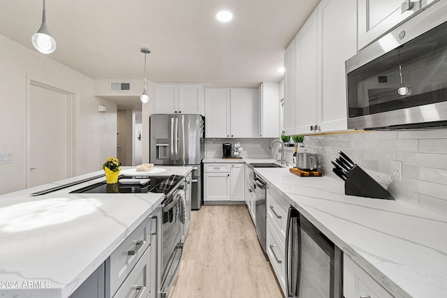 kitchen featuring light stone countertops, pendant lighting, stainless steel appliances, and white cabinetry