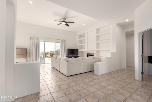 unfurnished living room with a tile fireplace, ceiling fan, built in features, and light tile patterned floors