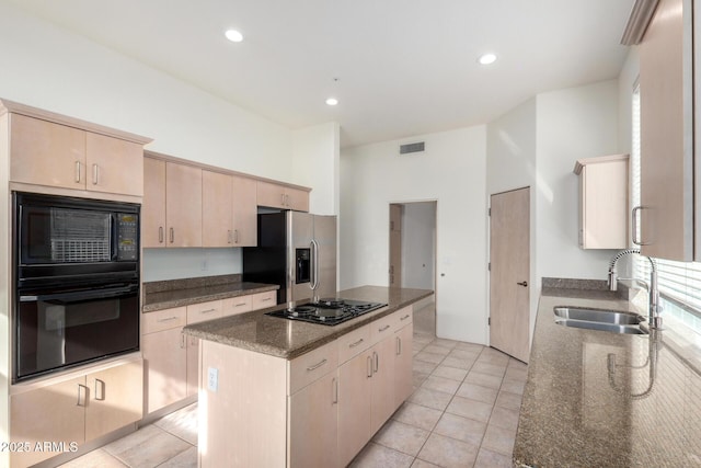 kitchen featuring dark stone counters, sink, black appliances, light brown cabinets, and a center island