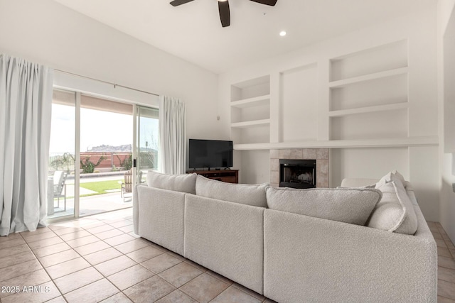 living room with a tiled fireplace, ceiling fan, built in features, and light tile patterned floors