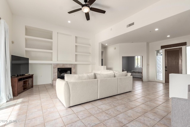 living room with built in shelves, ceiling fan, light tile patterned floors, and a tiled fireplace