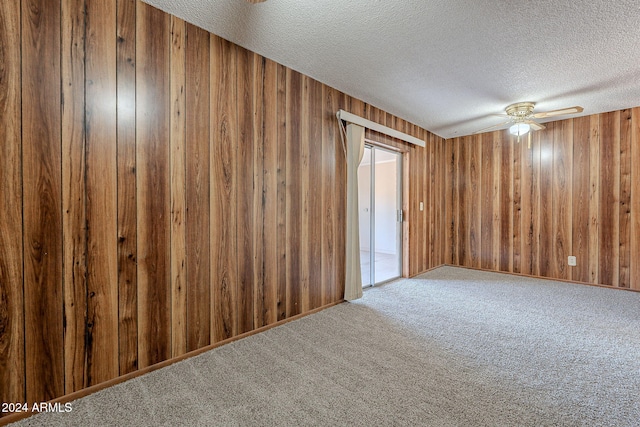 empty room featuring ceiling fan, carpet floors, a textured ceiling, and wooden walls