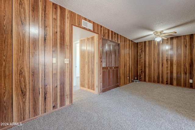 carpeted spare room featuring ceiling fan, a textured ceiling, and wooden walls