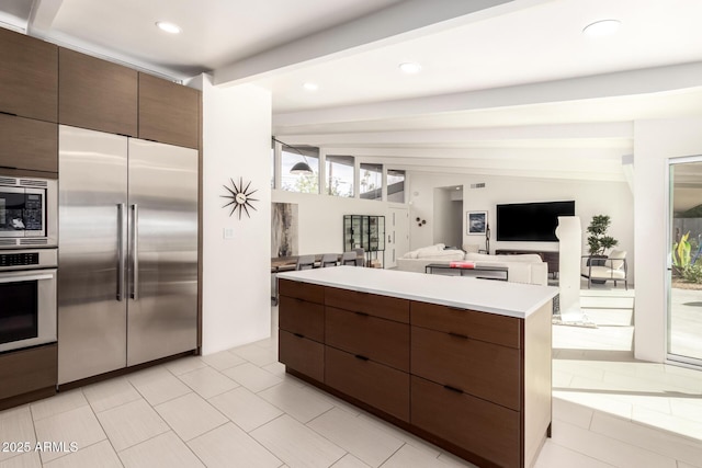 kitchen featuring light countertops, built in appliances, modern cabinets, a center island, and beamed ceiling