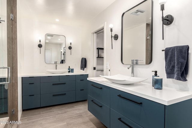 bathroom featuring visible vents, wood finished floors, a sink, and two vanities
